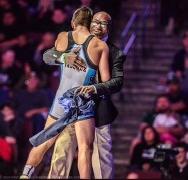 A coach in a suit embracing a wrestler after a match