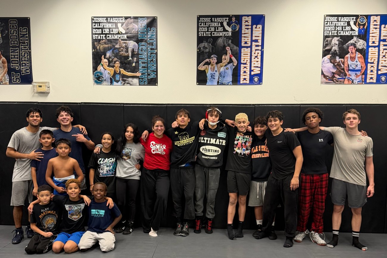 Athletes and a coach standing beneath state champion banners on the wall of the home gym