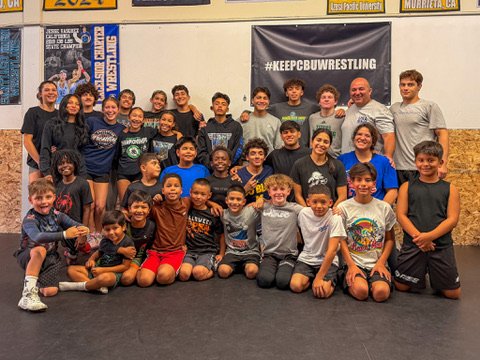 Athletes and coaches posed together in front of a Keep CBU Wrestling banner