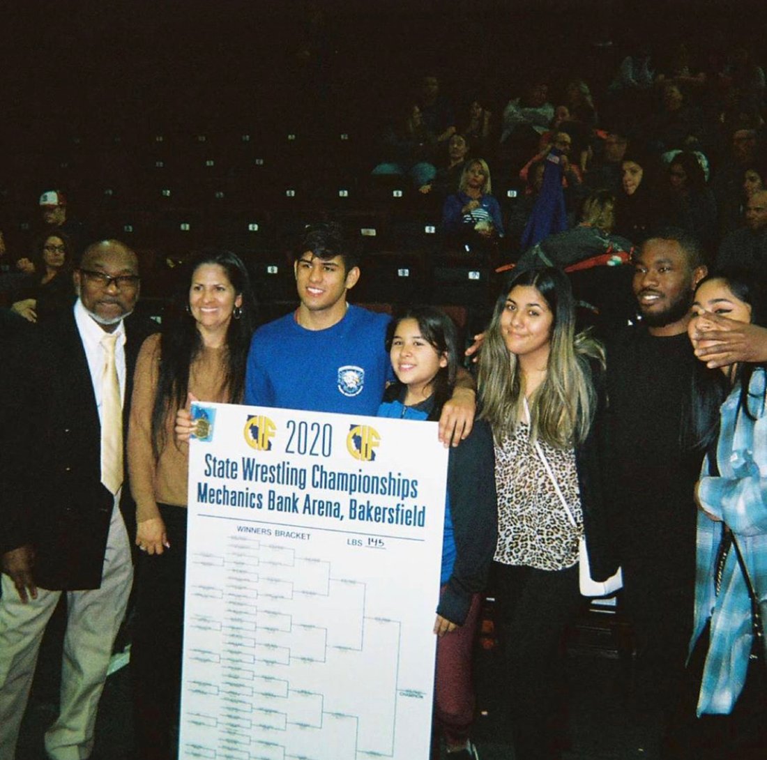 A wrestler with family and his coach holding the 2020 CIF state championship bracket
