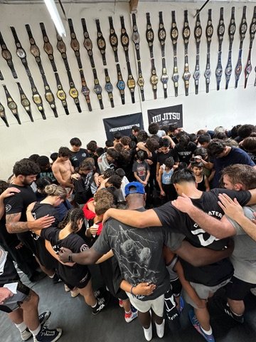 Athletes and coaches in a team huddle beneath a wall of championship belts