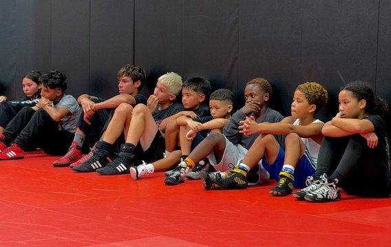 Young wrestlers sitting on the mat listening to their coach